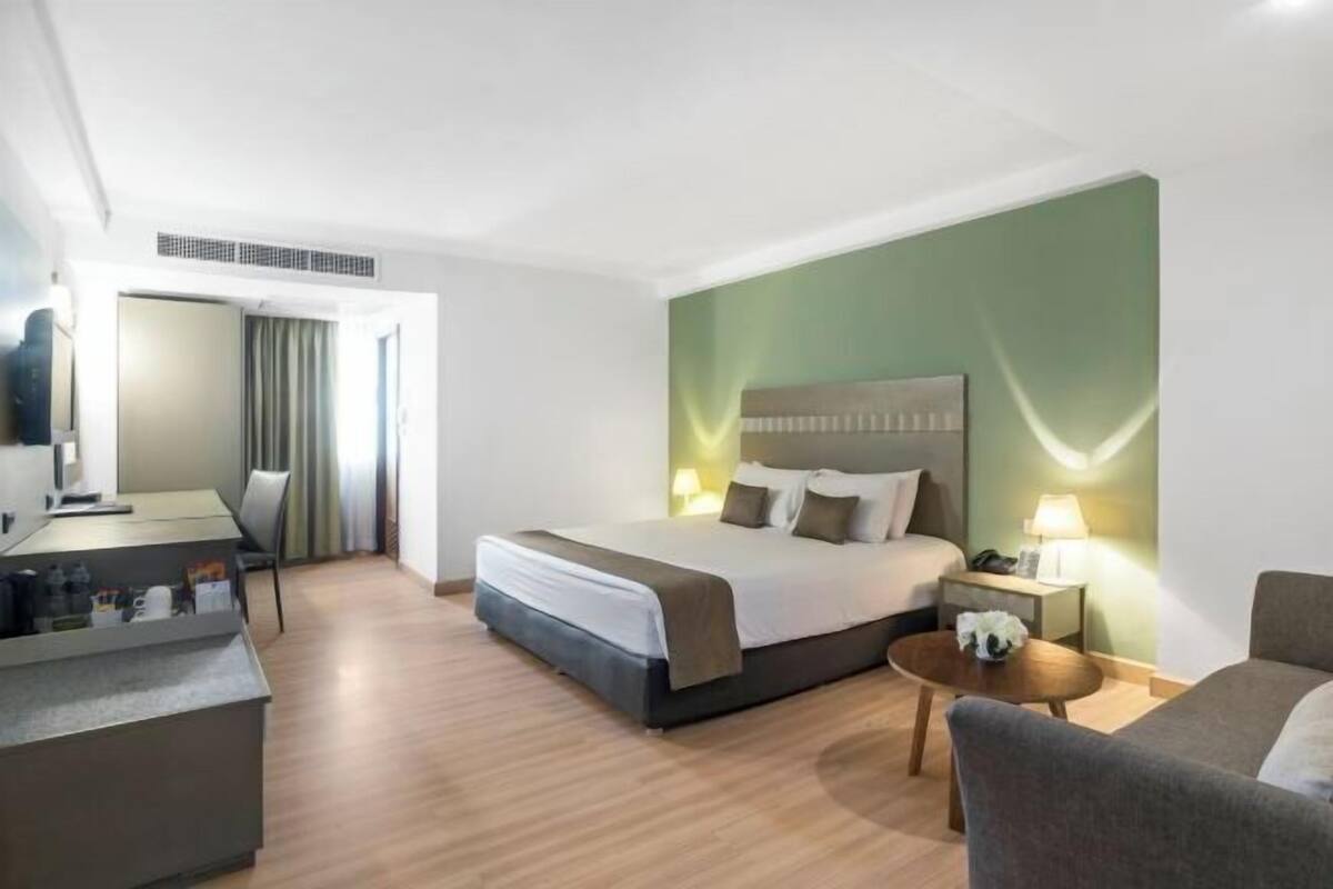 A hotel room with a bed, a desk, a chair, a sofa, and a small table.
