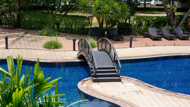 A swimming pool with a bridge, lounge chairs, and surrounding greenery. - SC Park Hotel (Bangkok)