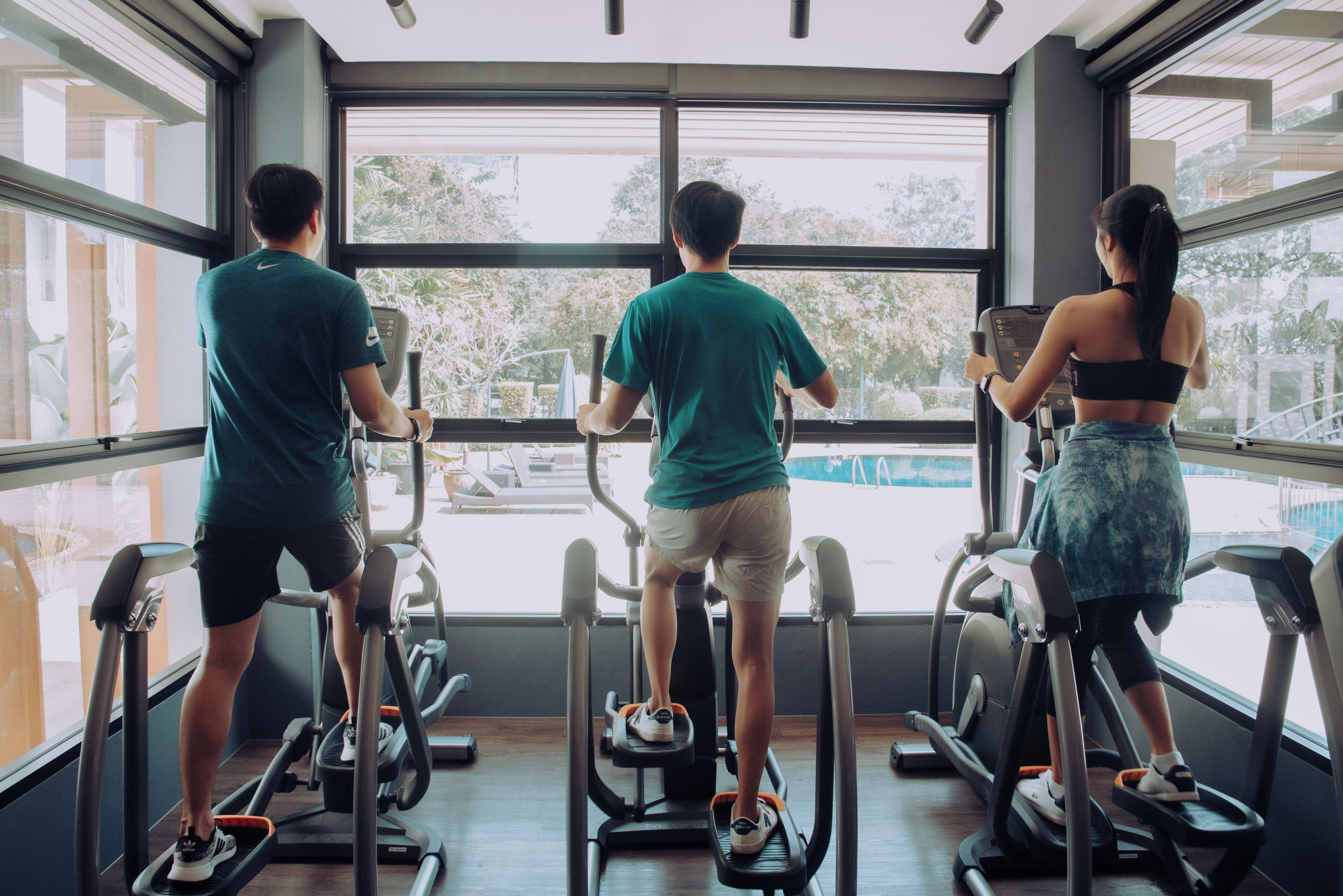 Tre persone che corrono su tapis roulant in una palestra con ampie vetrate.