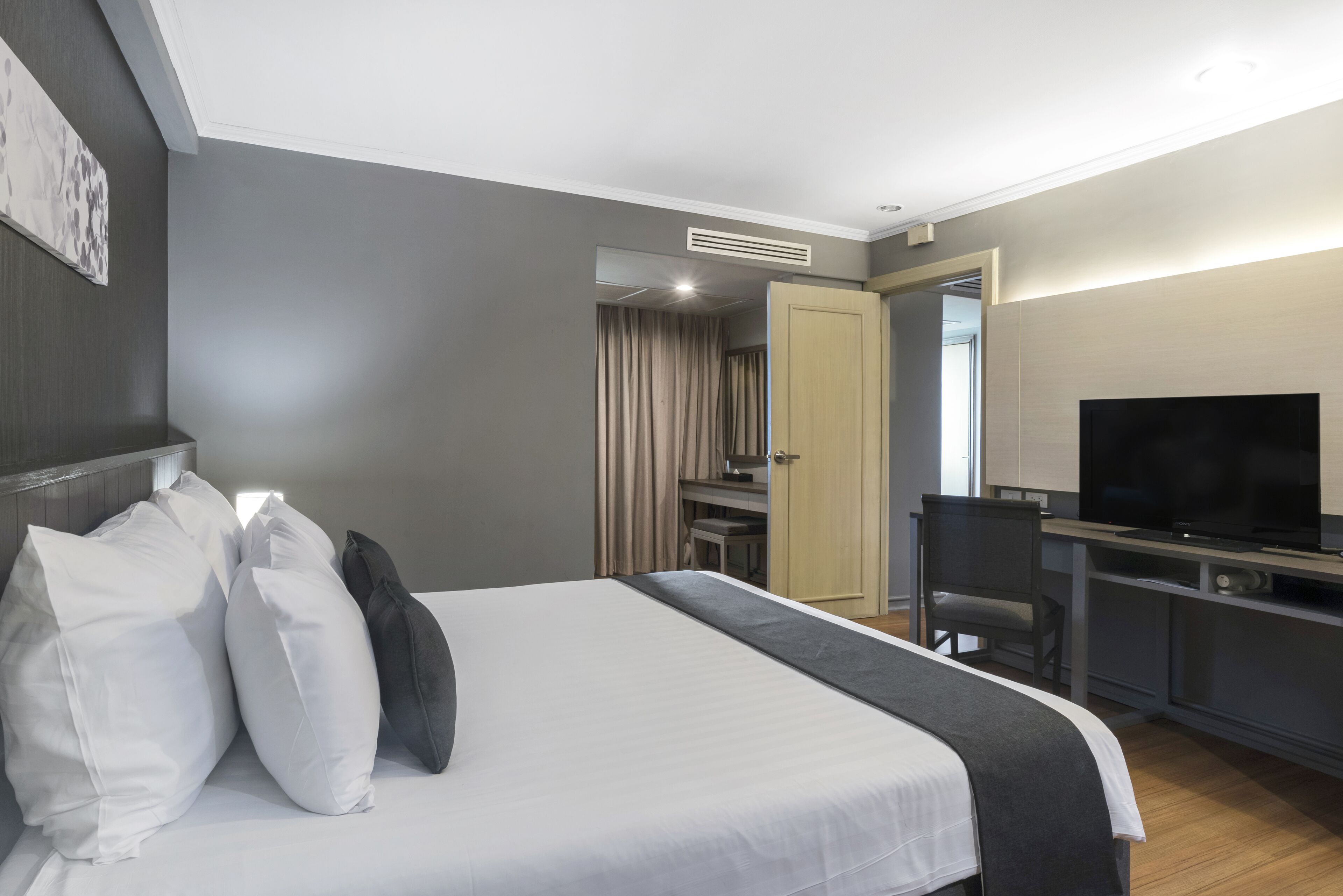 A hotel room with a bed, a desk, a TV, and a bathroom visible through an open door.