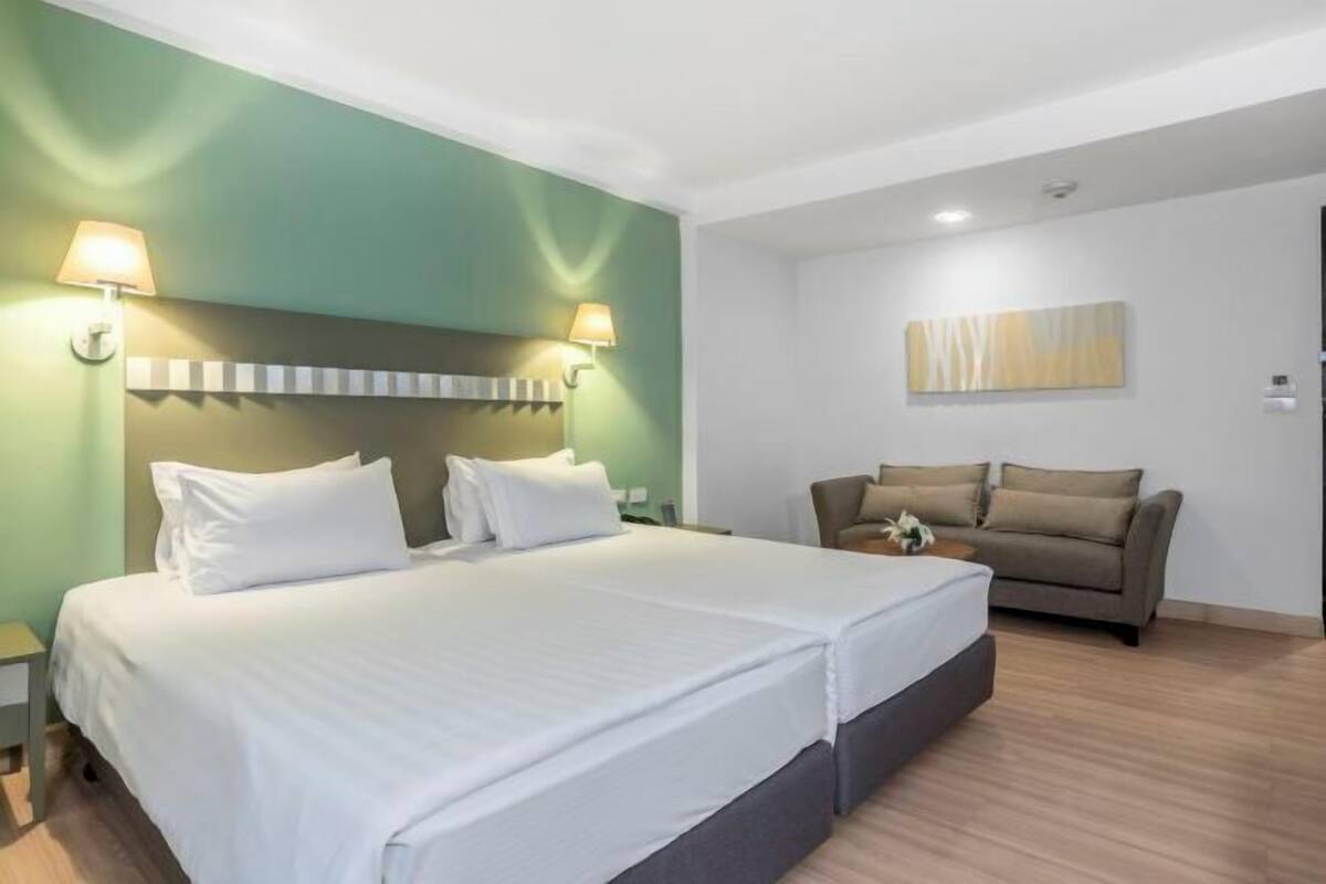 A hotel room with a large bed, a sofa, and two wall-mounted lamps.