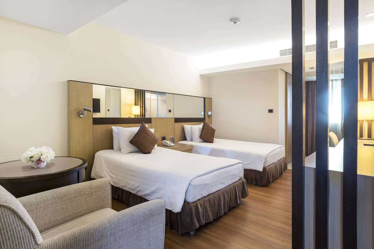 A hotel room with two beds, a round table with a vase of flowers, a sofa, and a large mirror on the wall.