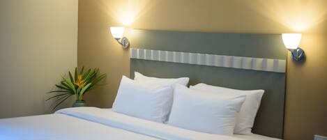Una cama bien tendida con sábanas blancas, cabecera con panel de color claro y dos lámparas fijadas a la pared.