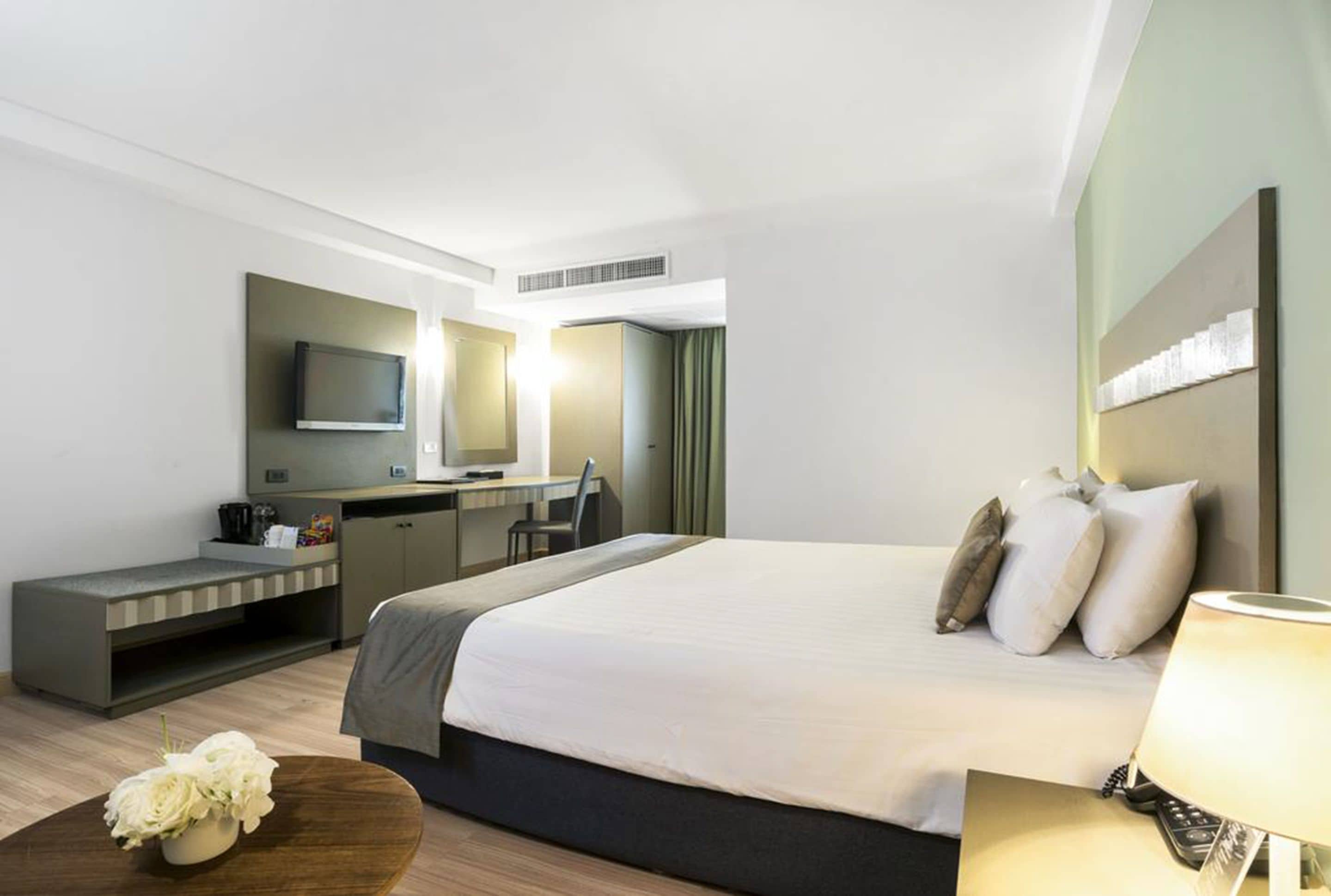 A hotel room with a bed, a desk, a chair, a TV, and a mirror.