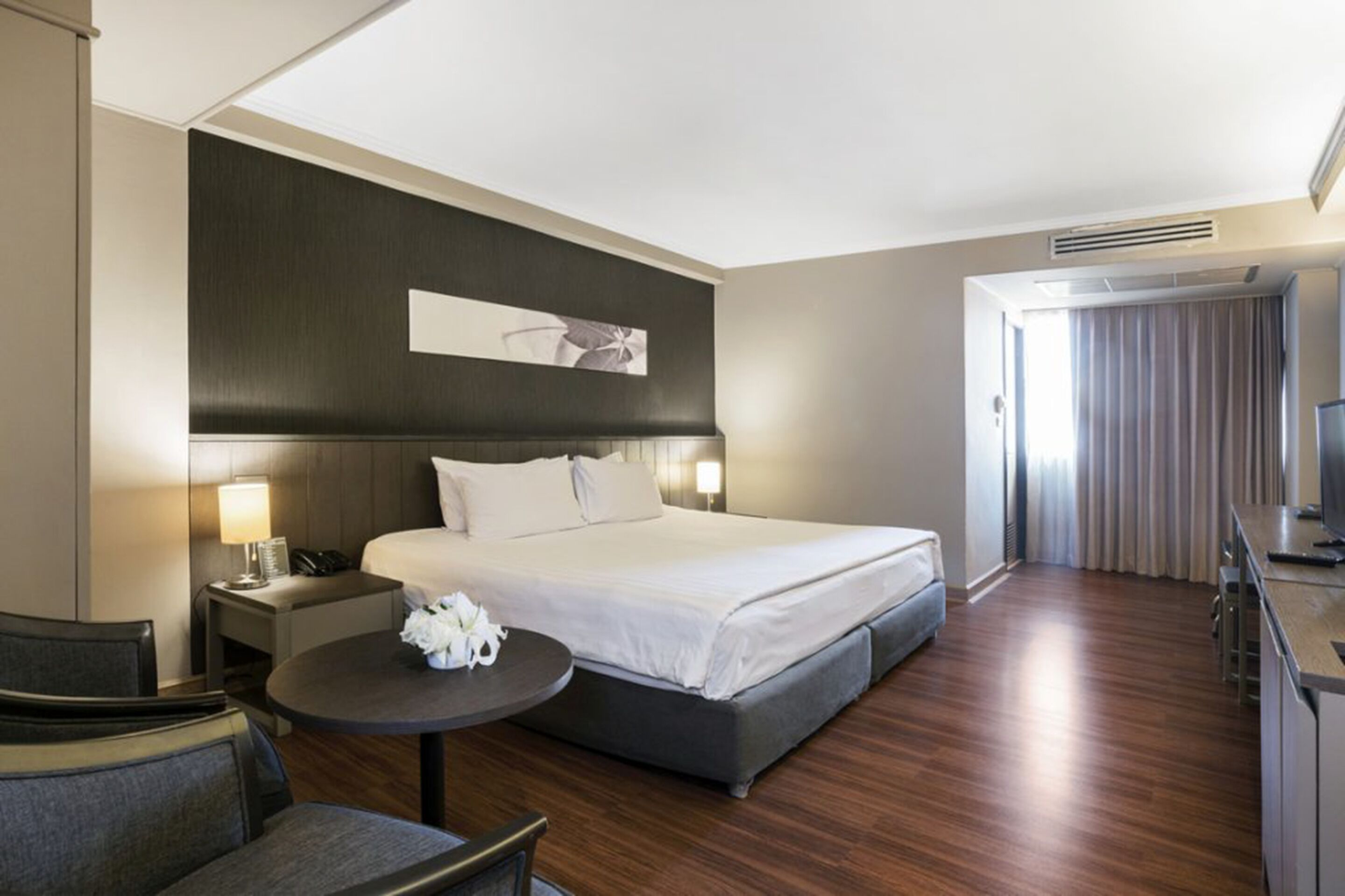 Ein modernes Hotelzimmer mit einem großen Bett, Nachttischen, einem kleinen runden Tisch und einer Sitzecke.