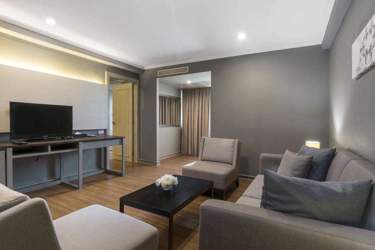 A modern living room with a flat-screen TV, a sofa, a coffee table, and a dining area with a table and chairs.