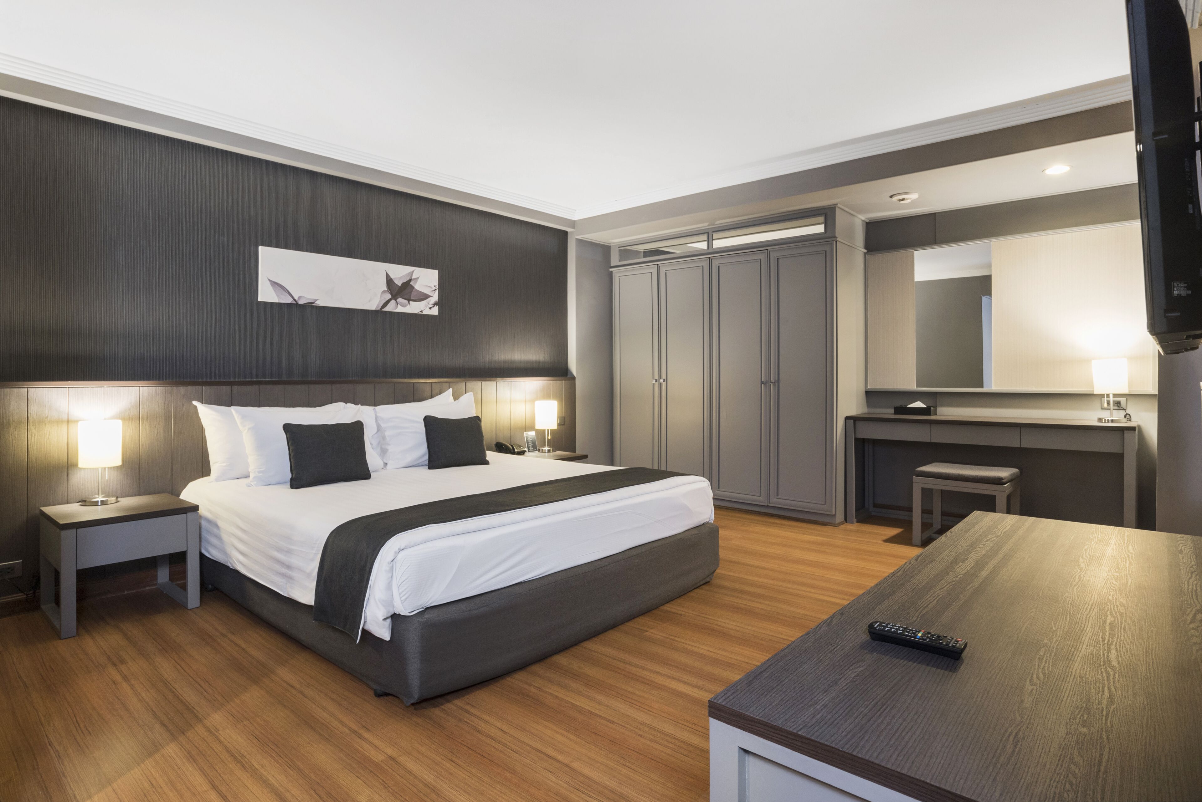 A modern hotel room with a large bed, bedside lamps, a desk, a TV, and a wardrobe.