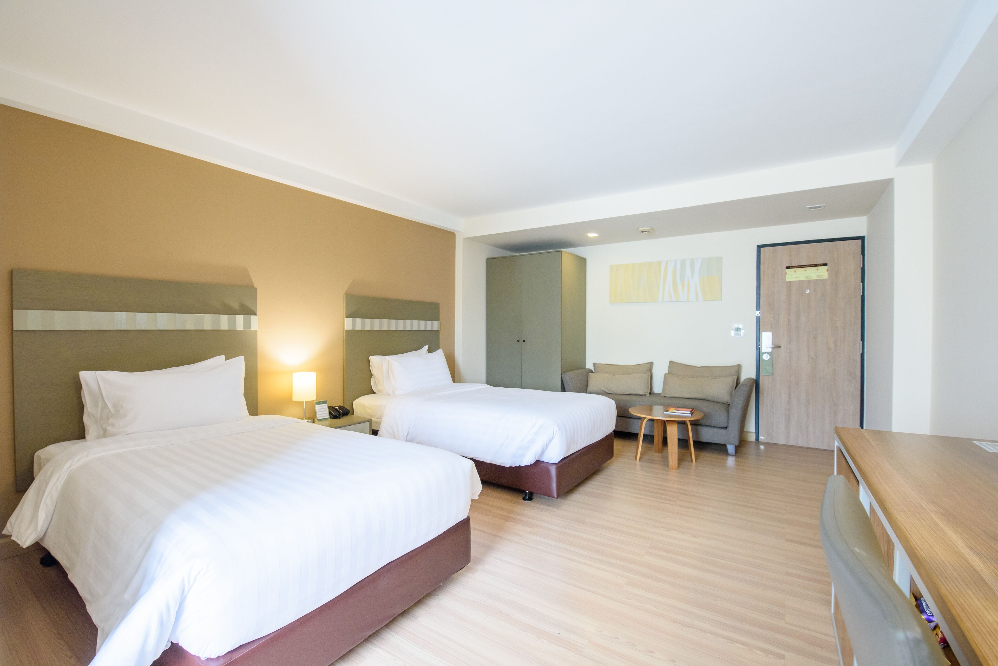 Una habitación de hotel con dos camas, un sofá, una mesita y un aparador de madera.