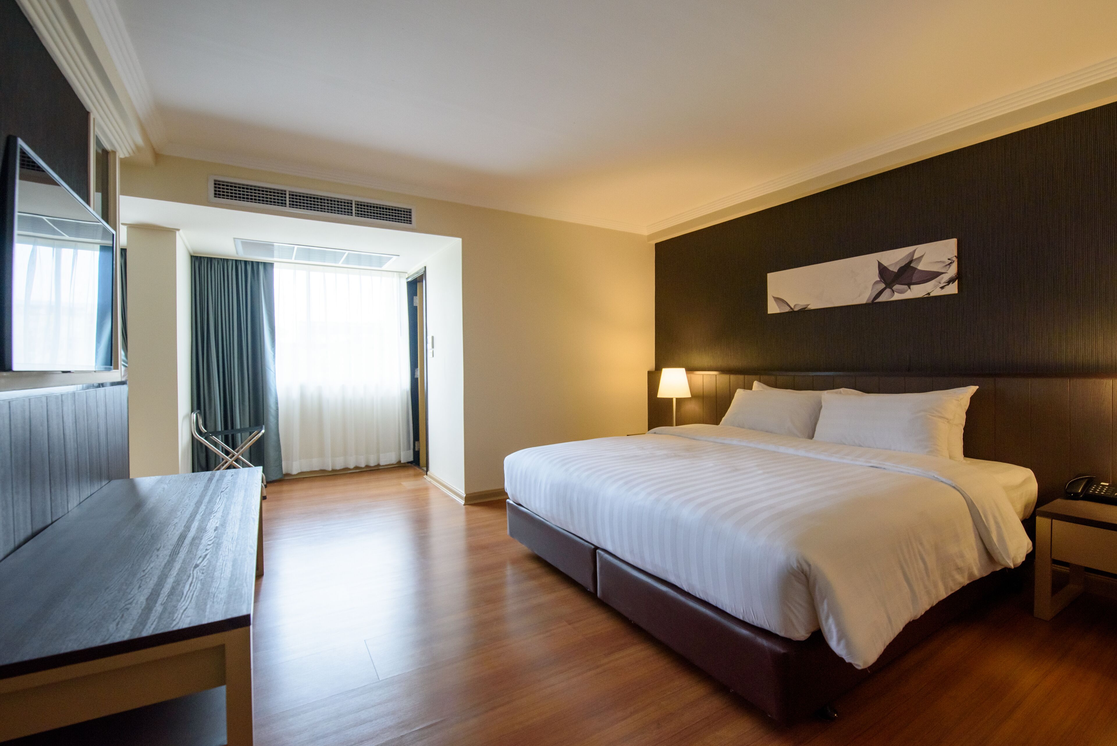 A hotel room with a bed, bedside table, lamp, and artwork on the wall.