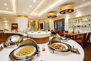 A buffet area with various food stations, a central serving counter, and a dining area with tables and chairs.