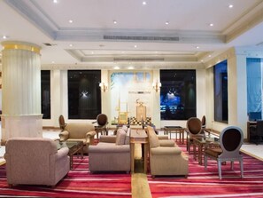 A hotel lobby with a central seating area, large windows, and a decorative chandelier.