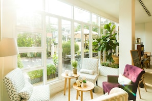 A bright room with large windows, a sofa, a chair, a small table, and a potted plant. - Hotel De Bangkok (Bangkok)