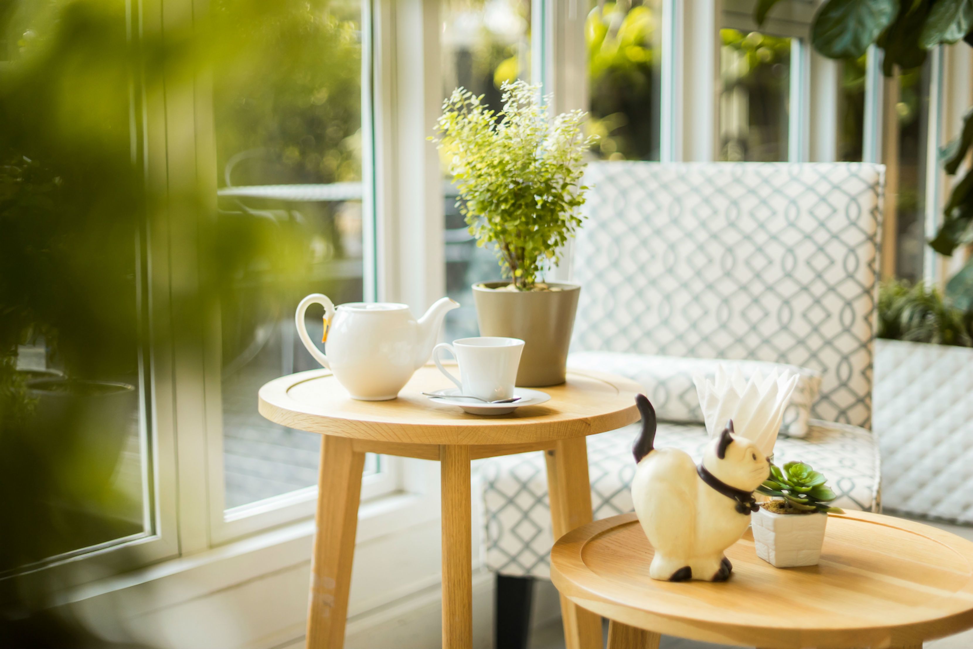 A cozy indoor setting with a round wooden table, a white teapot, a cup, and a small potted plant.