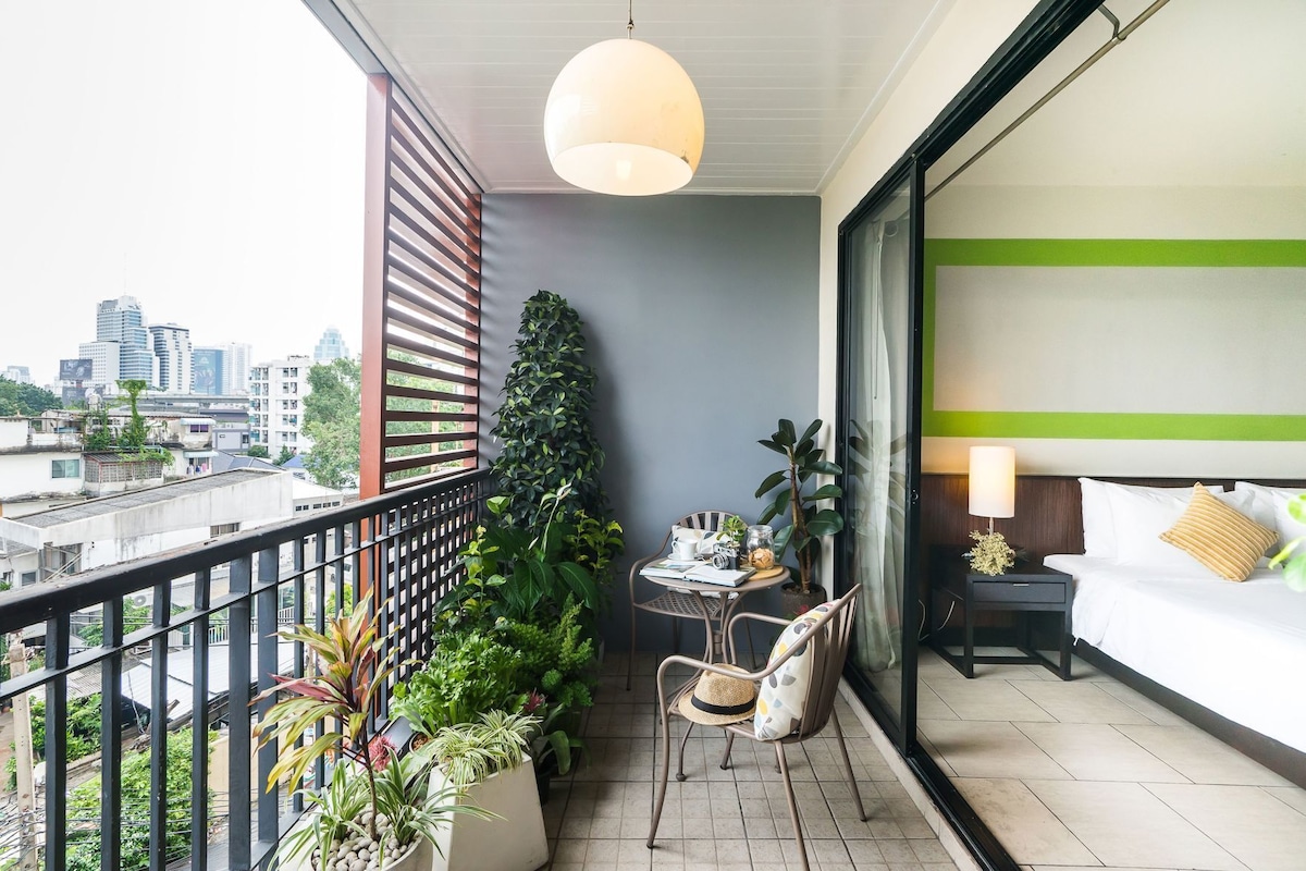 Ein Balkon mit Blick auf die Stadt, ein Tisch mit Stühlen, ein Blumentopf und ein Bett mit Kissen.