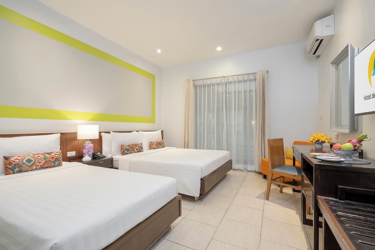 Une chambre d’hôtel avec deux lits, un bureau et une chaise. Il y a une fenêtre avec des rideaux, un climatiseur fixé au mur et un tableau encadré accroché au mur.