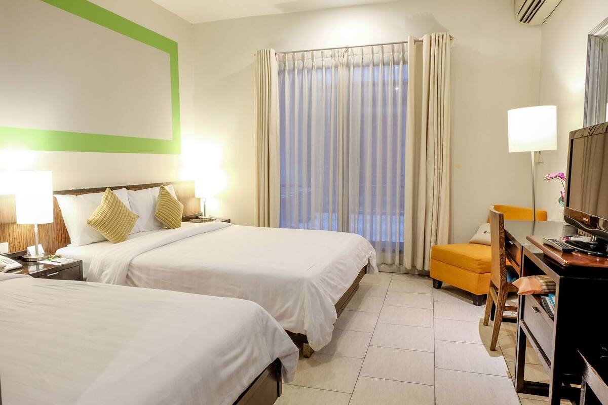 Une chambre d’hôtel avec deux lits, un bureau équipé d’un ordinateur, une chaise et un téléviseur.