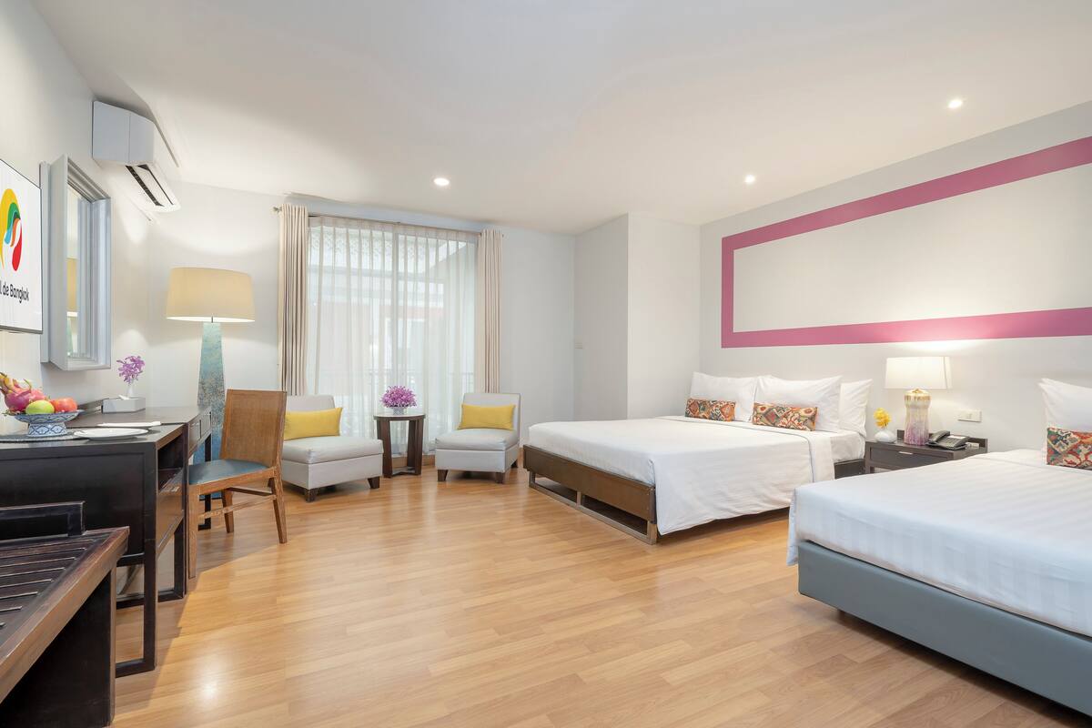 Une chambre d’hôtel avec deux lits, un bureau, une chaise, une petite table avec une lampe et une fenêtre avec des rideaux.