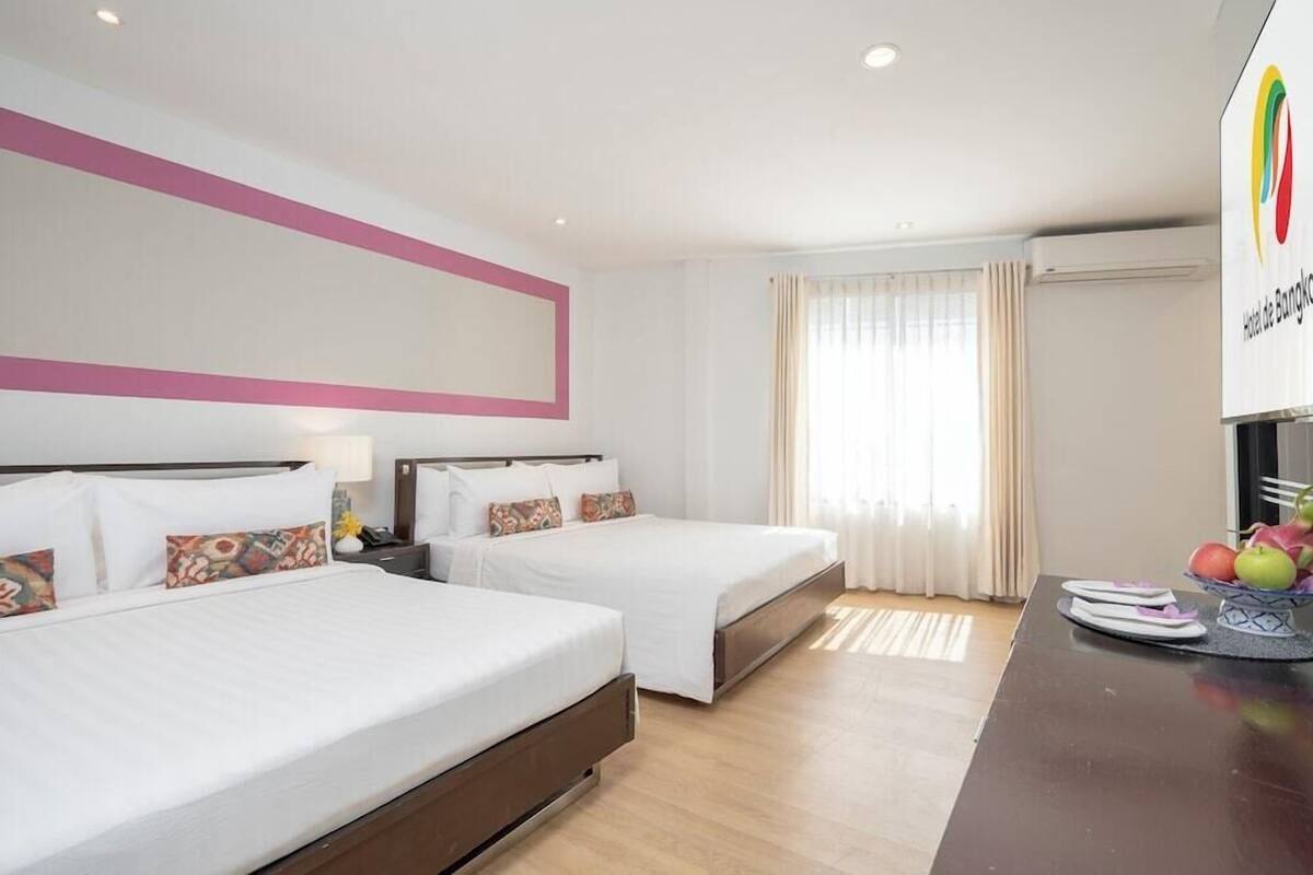 Une chambre d’hôtel avec deux lits, une table à manger avec des fruits et une grande fenêtre avec des rideaux.