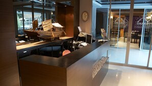 A reception desk with a wooden ship model, a clock, and a glass door leading to a dining area. - Grand Pinnacle (Bangkok)