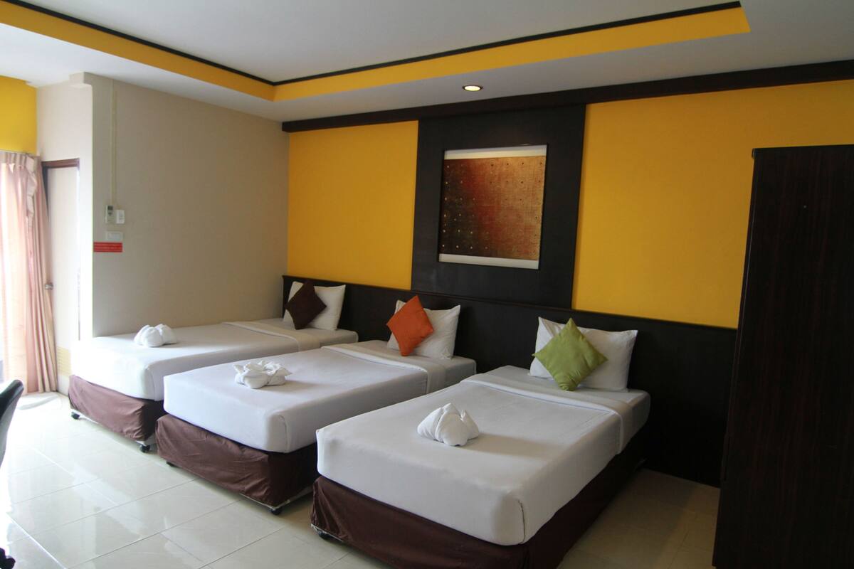 A hotel room with three single beds, each with a pillow and a towel.