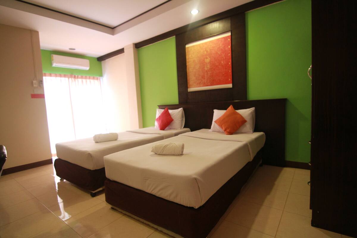 A hotel room with two beds, each with white linens and pillows, a green accent wall, and a large painting above the beds.