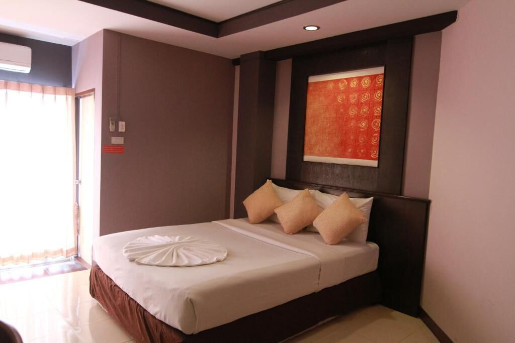 A hotel room with a large bed, a headboard with a decorative panel, and a window with curtains.