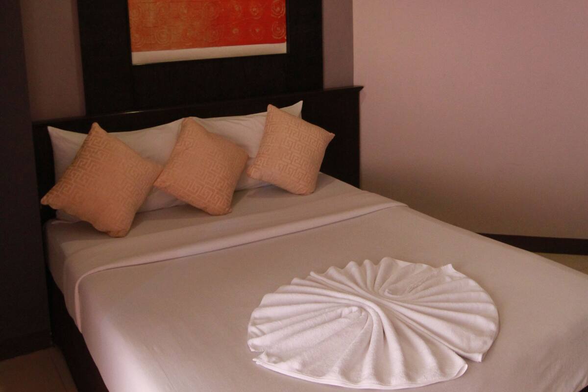 A hotel room with a neatly made bed, a large painting on the wall, and a modern ceiling design.