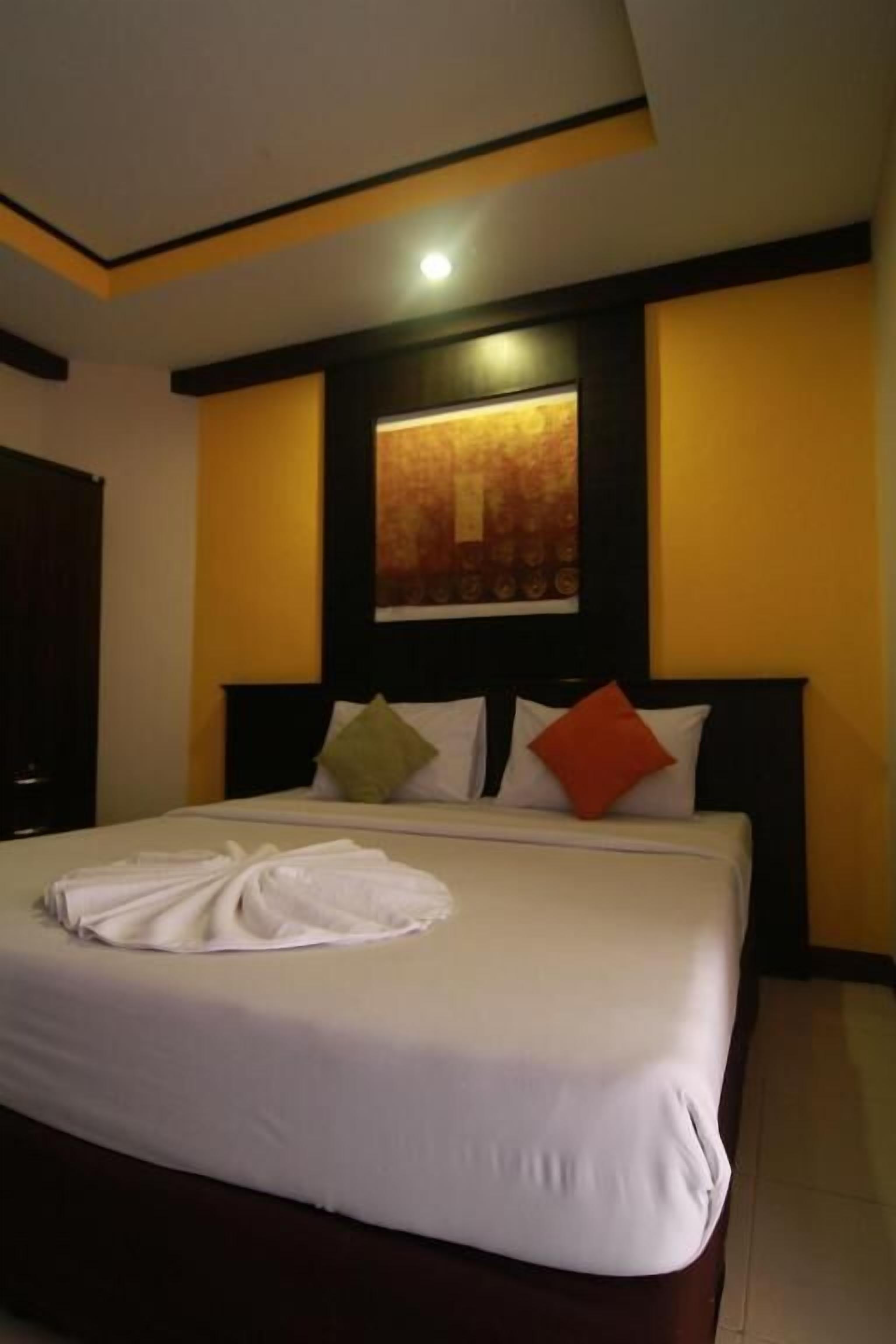 A neatly made bed with white linens and a folded towel, a dark headboard, and a wall-mounted artwork above it.