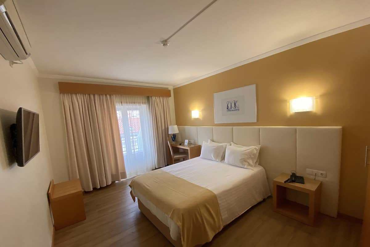 Habitación de hotel con una cama grande, un escritorio, una silla, un televisor de pantalla plana y un ventanal con cortinas.