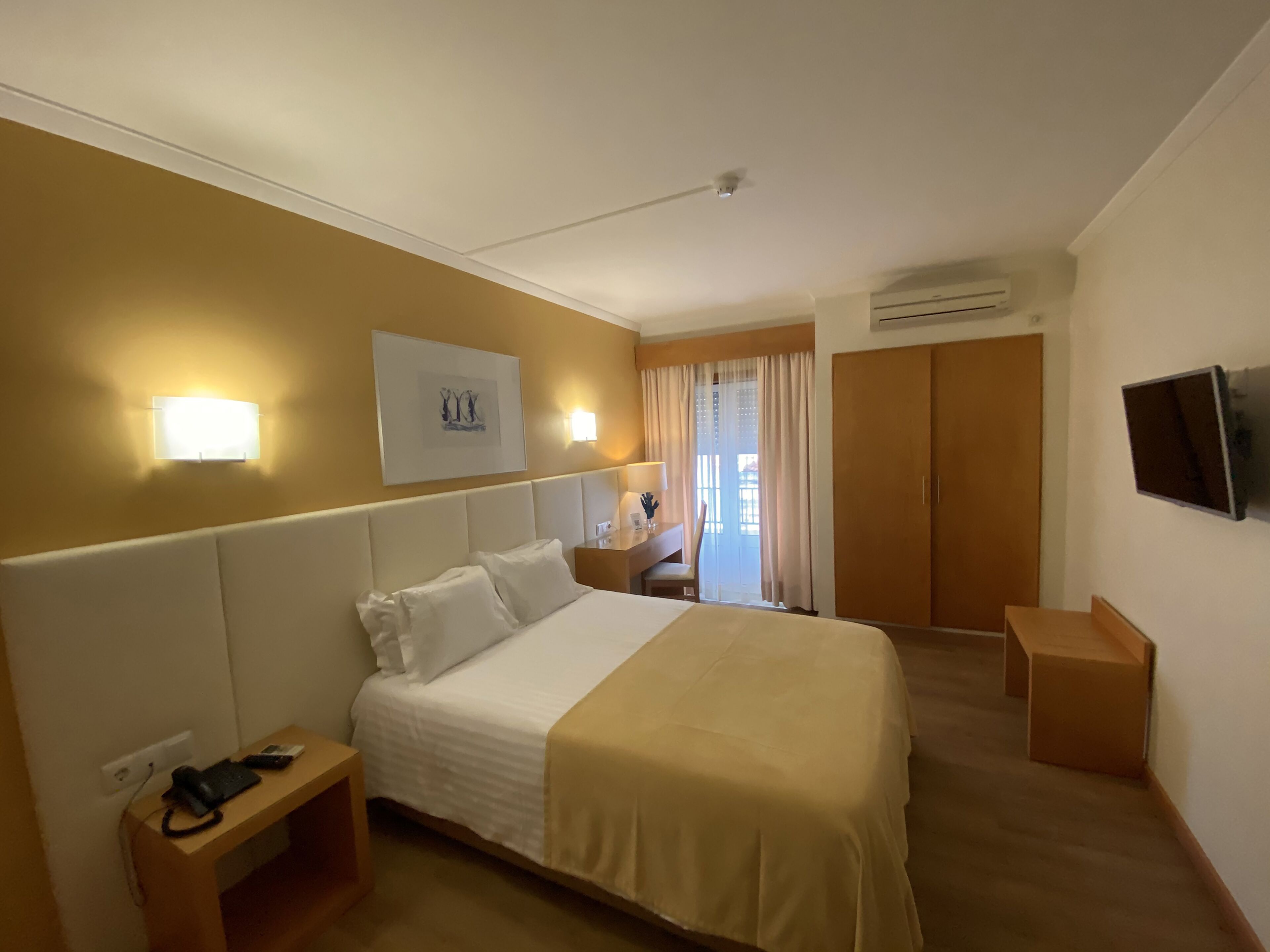 Une chambre d’hôtel avec un grand lit, des tables de chevet, un bureau, une chaise, une télévision et un appareil de climatisation.