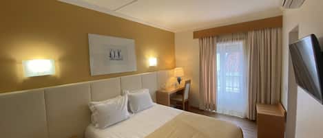 Una habitación de hotel con cama, mesita de noche, lámpara, escritorio, silla y televisor.