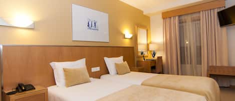 A hotel room with two beds, a bedside table with a phone, a mirror, a TV, and a framed picture on the wall.