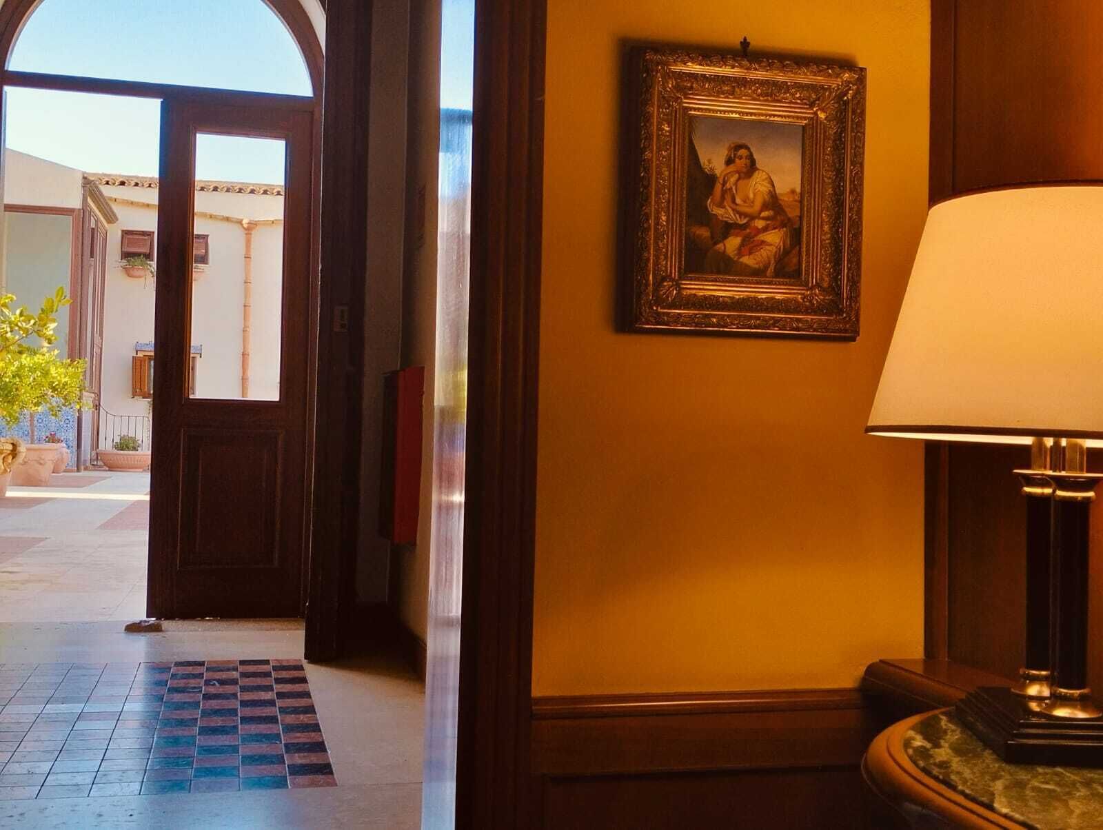 A hotel lobby with a wooden door, a framed painting on the wall, and a lamp.