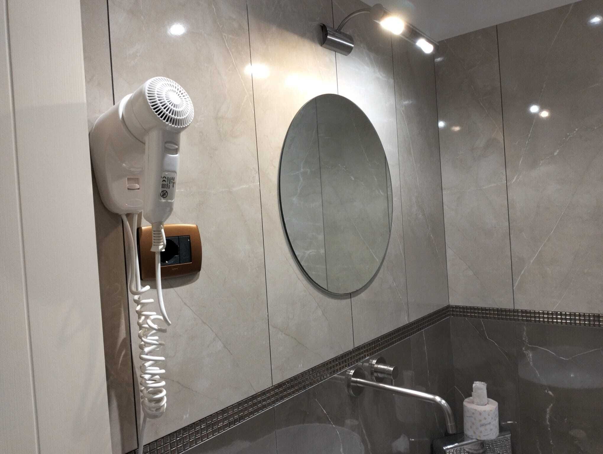 A bathroom with a hairdryer, a round mirror, and a towel dispenser.