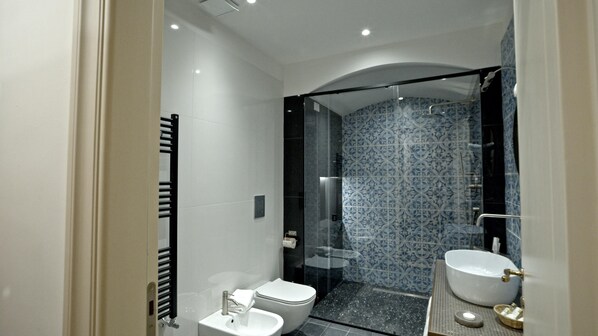 A modern bathroom with a glass-enclosed shower, a white toilet, and a large sink with a gold faucet. - Baglio Della Luna (Agrigento)