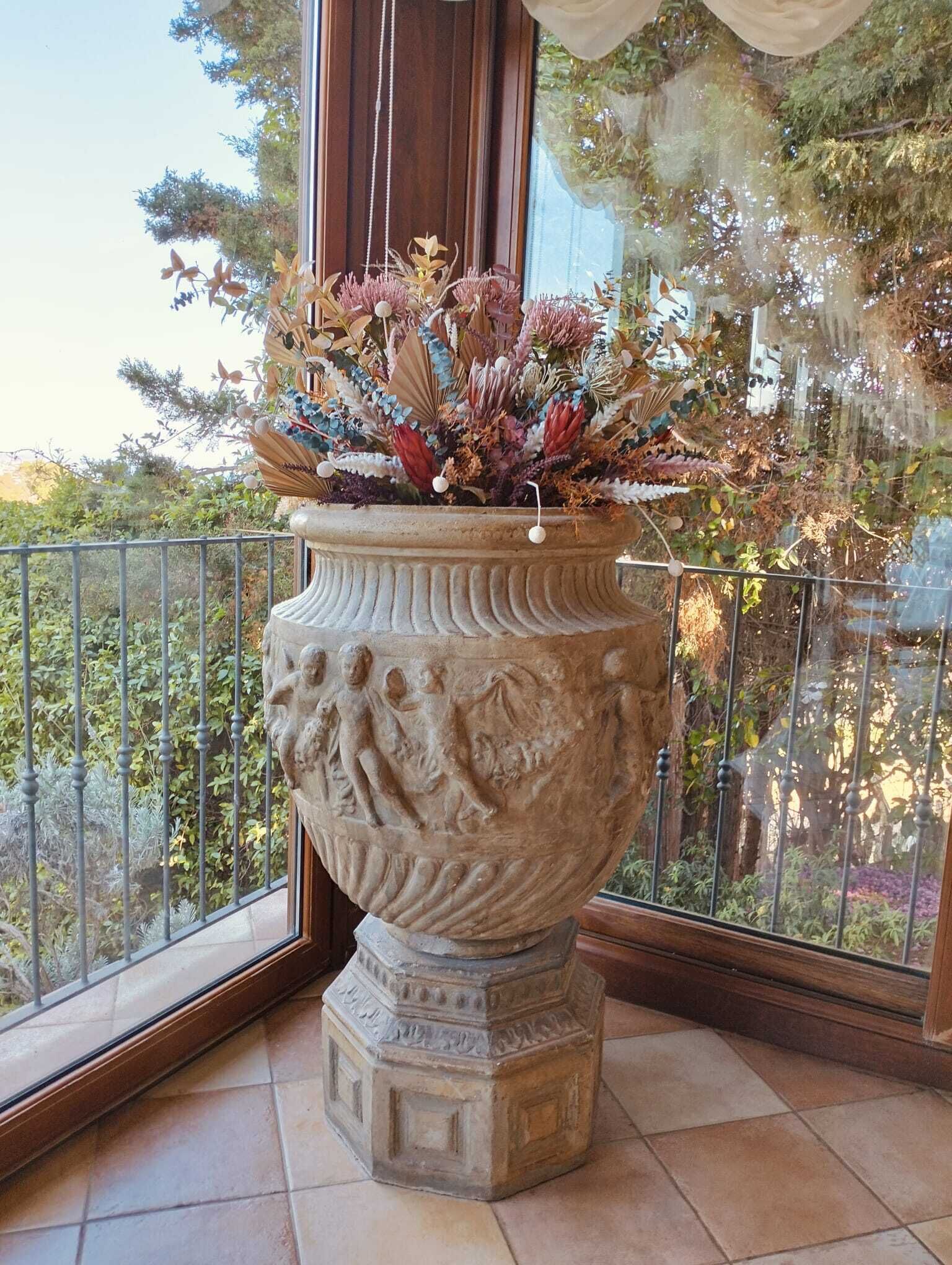 A large, ornate planter with a classical design, placed on a balcony with a metal railing.