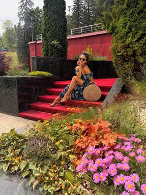 A woman sitting on red steps in a garden with various plants and flowers. - Hotel Piatra Mare (Brasov)