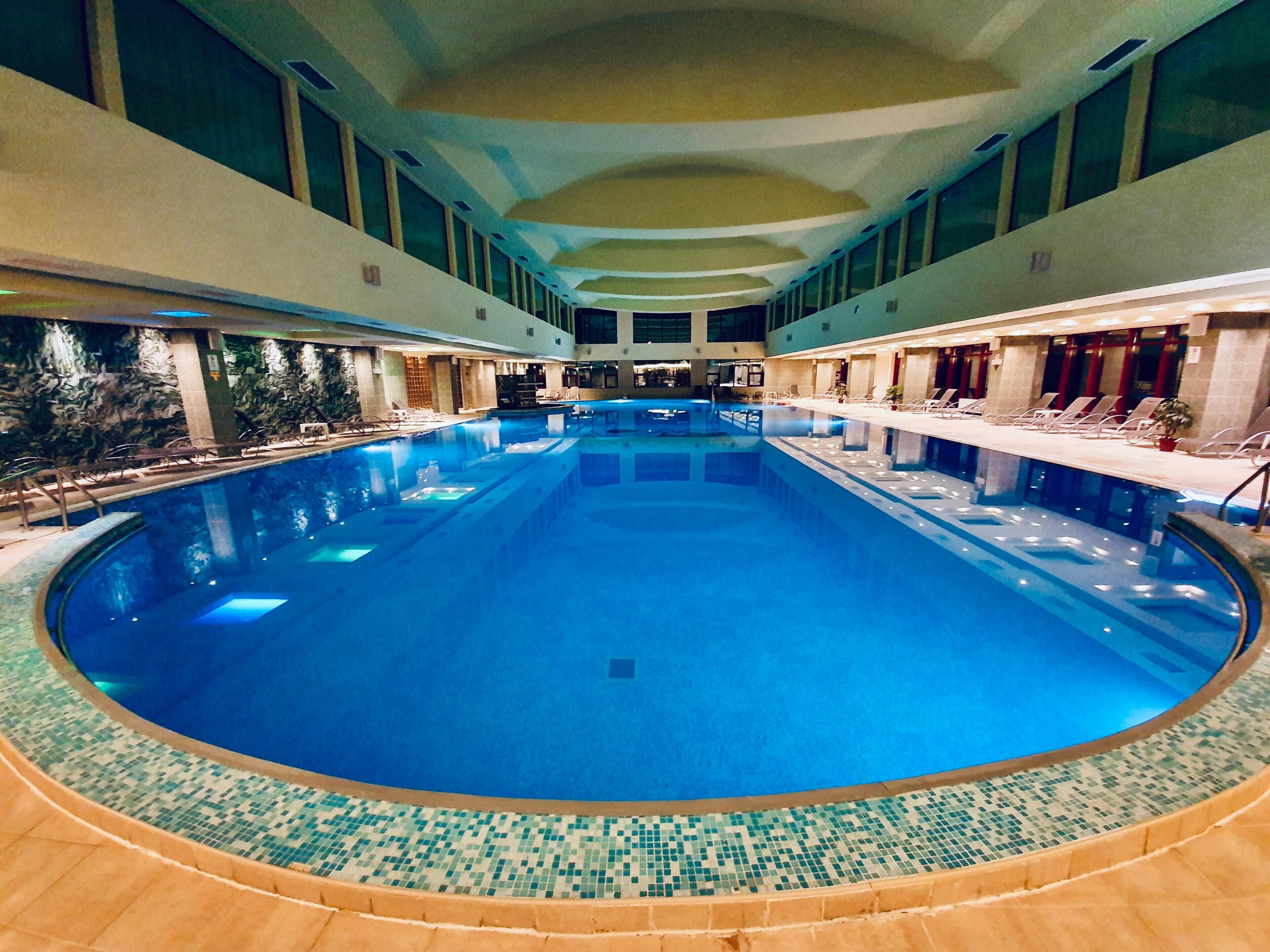 Ein großer, überdachter Swimmingpool mit gefliestem Rand, umgeben von Liegestühlen und einer Bar.