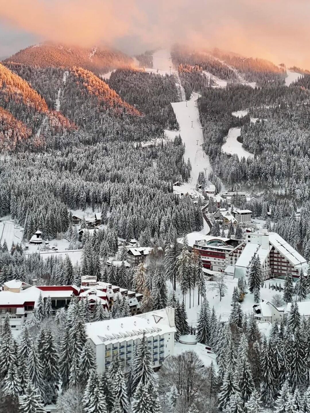 A snow-covered mountainous area with a ski resort, including buildings and ski lifts.