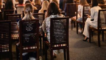 A conference room with rows of wooden chairs, a projection screen, and a presentation in progress.