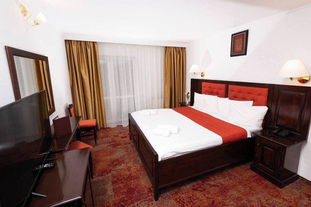 Une chambre d’hôtel avec un grand lit, un bureau avec un ordinateur portable, une télévision et une table de chevet avec une lampe.