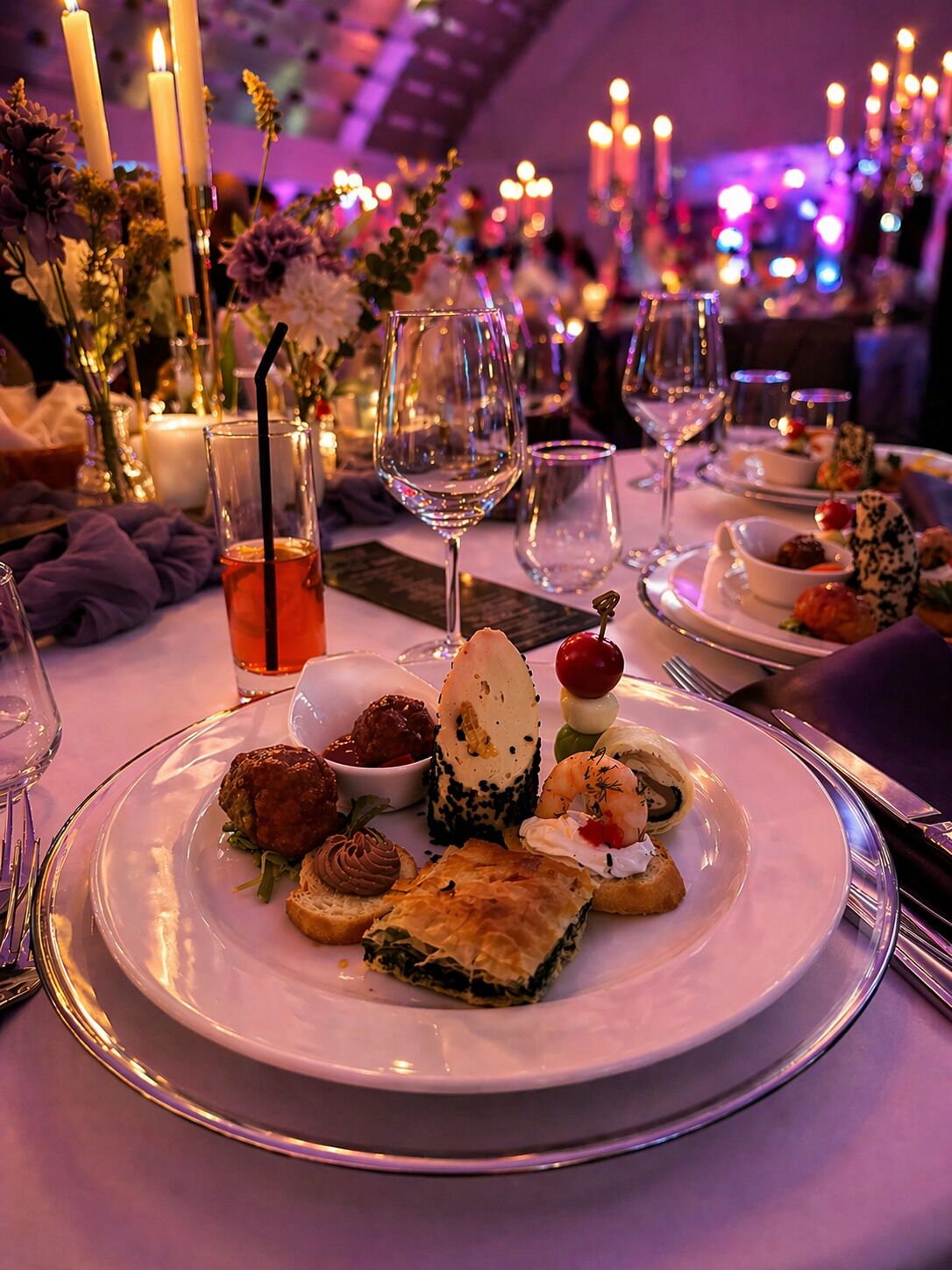 A dining table with plates of food, glasses of wine, and candles.