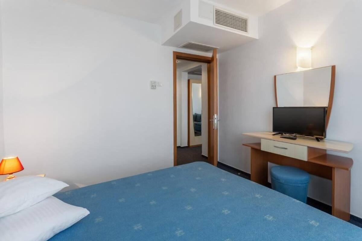 A hotel room with a bed, a desk with a TV, a lamp, and a mirror.