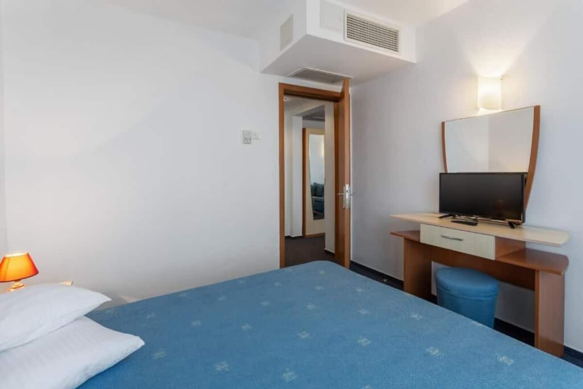 A hotel room with a bed, a desk with a TV, a lamp, and a mirror.
