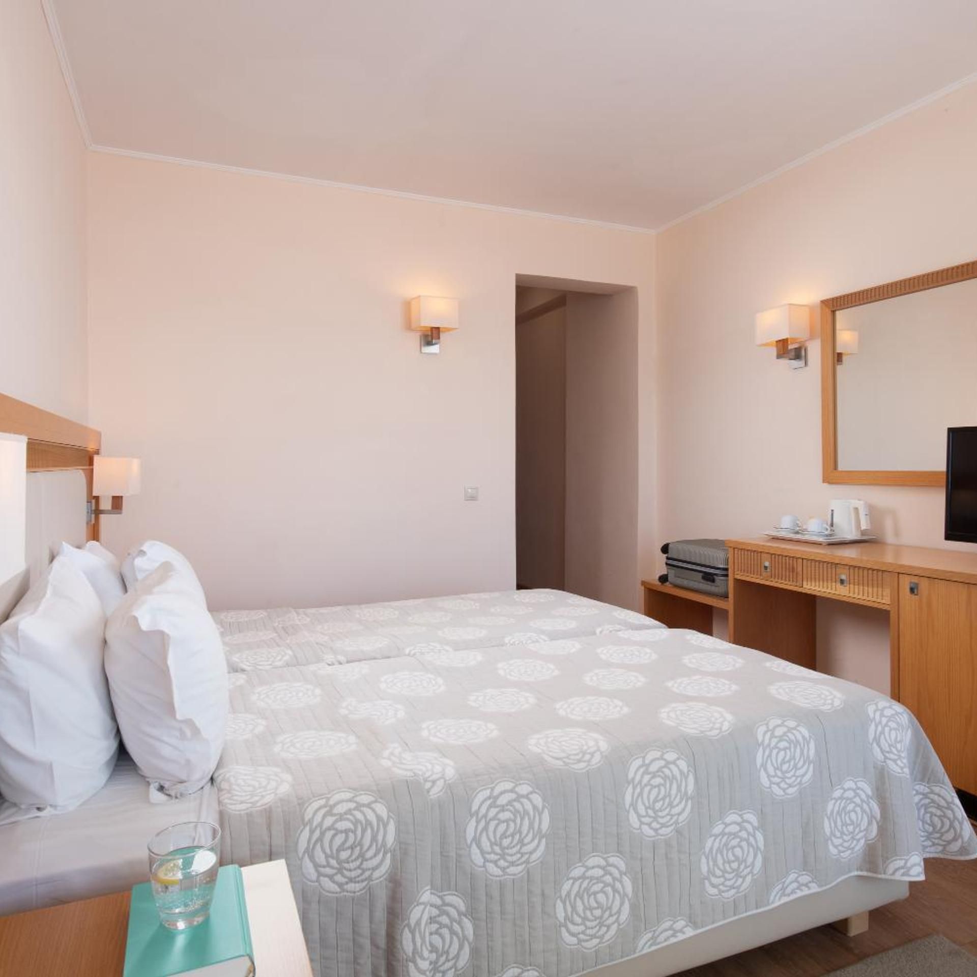 A hotel room with a bed, bedside table, lamp, and a desk with a mirror.