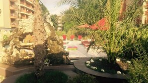 A landscaped outdoor area with a rock formation, palm trees, and a paved pathway. - Hotel Bahami Residence (Sunny Beach)