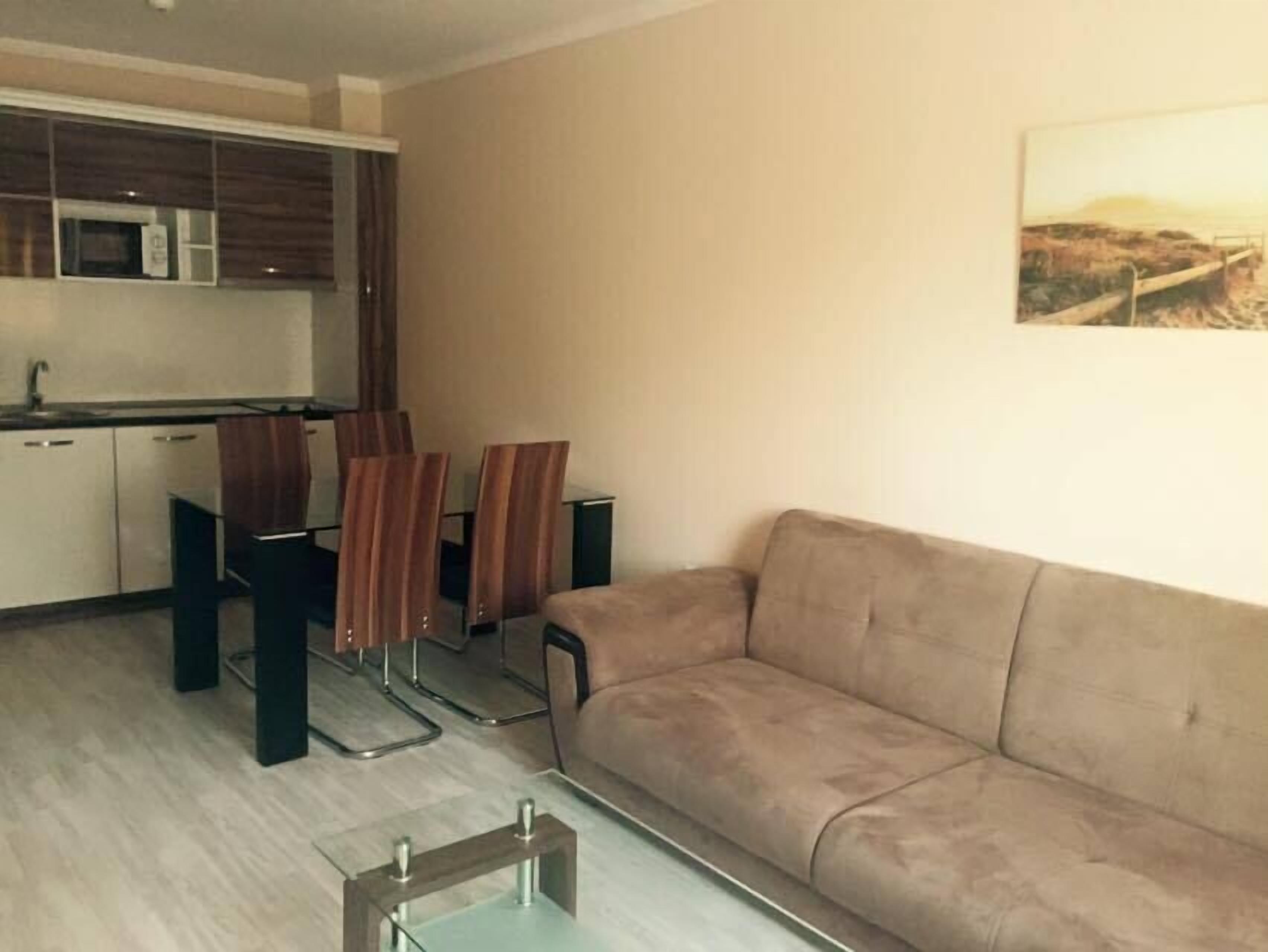 A living room with a beige sofa, a dining table with four chairs, and a kitchen area with cabinets and a microwave.