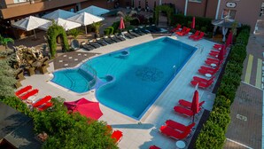 A hotel pool area with sun loungers and umbrellas, surrounded by greenery and a building with balconies. - Hotel Bahami Residence (Sunny Beach)