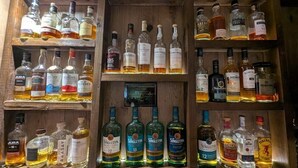 A wooden liquor cabinet with various bottles of alcohol, including brands like JURA, Glenlivet, and Talisker. - The Bog Roy Inn (Inverness)