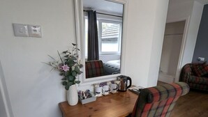 A wooden dresser with a mirror above it, a plaid chair, and a small plant beside the dresser. - The Bog Roy Inn (Inverness)